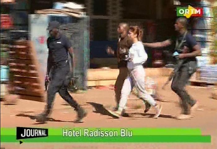 In this TV image taken from Mali TV ORTM, a woman is led away by security personnel from the Radisson Blu Hotel  hotel in Bamako, Mali, Friday Nov. 20, 2015.  Men shouting "God is great" and armed with guns and throwing grenades stormed into the Radisson Blu Hotel in Mali's capital Friday morning. (Mali TV ORTM,  AP) MALI OUT